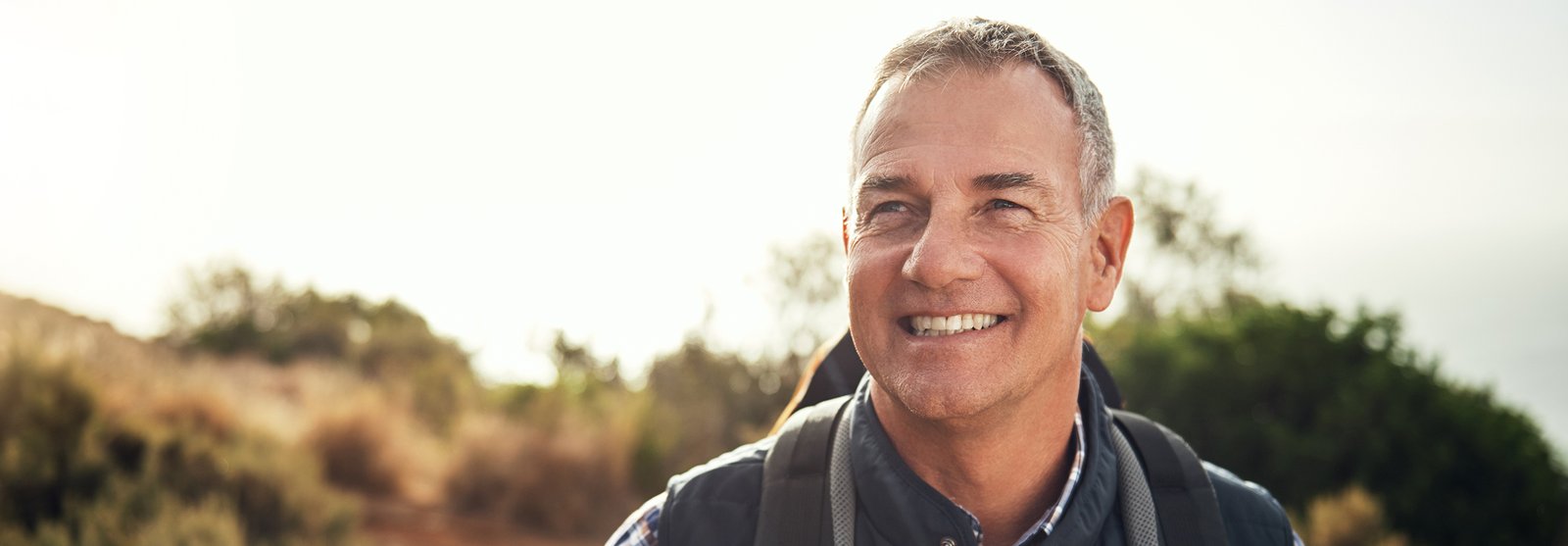 smiling man with backpack on a trail in the mountains