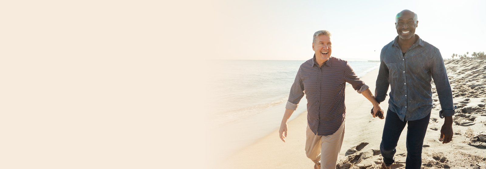 Two men holding hands and smiling at the beach